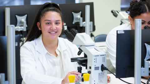 Student in a lab coat using a microscope