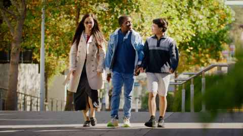 Three students walking outdoors on a sunny day