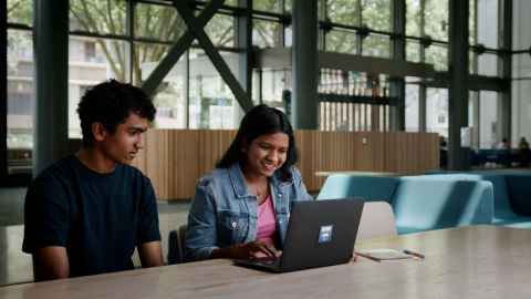Two students seated at a table working on a laptop