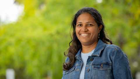 Smiling woman standing outdoors with greenery in the background