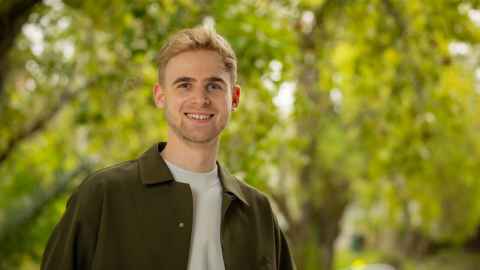 Smiling man standing outdoors with large, out of focus trees in the background