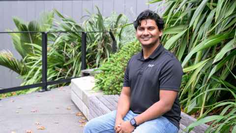 Man sitting on a wooden bench with flax and greenery in the background