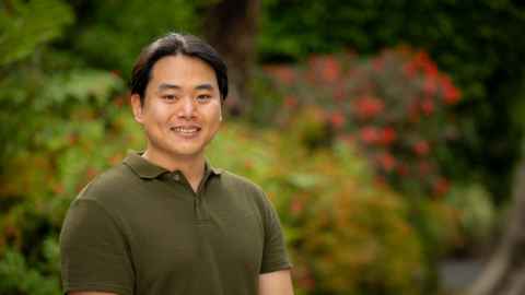 Smiling man standing outdoors in front of shrubs and trees