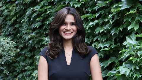A smiling young woman standing in front of a wall of greenery.