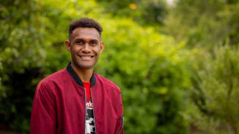 Smiling standing outdoors in front of shrubs and trees