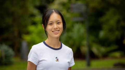 Smiling woman standing outdoors with greenery in the background