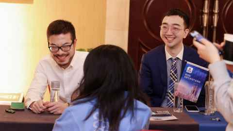 Two smiling men sitting at a table talking with a woman