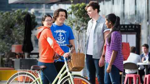 Four students standing and talking, one holding a bicycle
