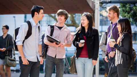 Five young people with backpacks standing around, talking.