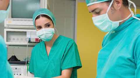 People in an operating theatre, wearing scrubs, masks and gowns.