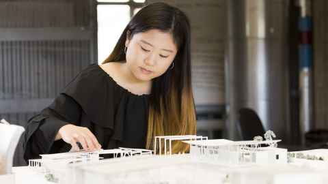 Student looking and touching small architectural models on desk