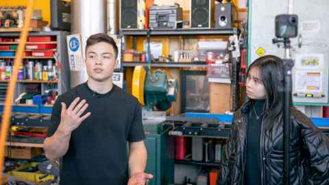 Two students stand inside a metal workshop on campus during the filming of the tour video.
