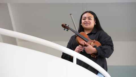 Anne Maroussia Filimoehala stands with her violin looking down from the internal balcony at the School of Music