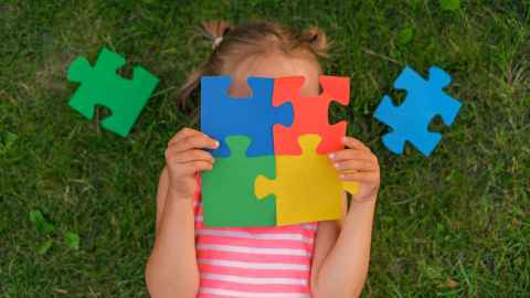A little girl with jigsaw pieces over her face.