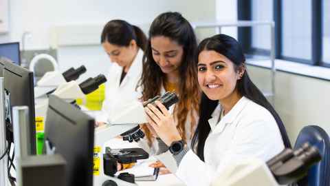 Three women in a lab with microscopes.
