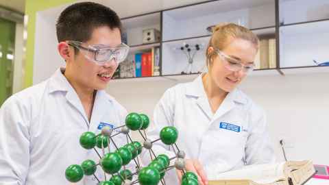 Two people in lab coats and protective eyewear in a lab.