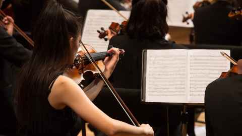 Violinists playing in an orchestra with sheet music in front of them.