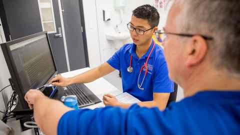 People looking at a computer screen, one with a stethoscope around his neck.