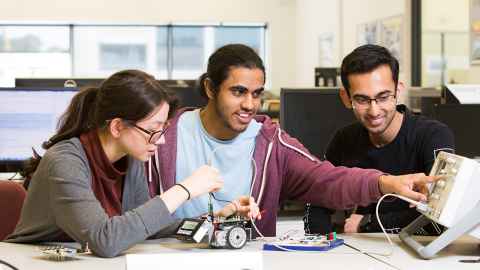 Three young people working with electronics.