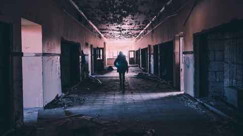 A dark figure walking down a dilapidated hallway.