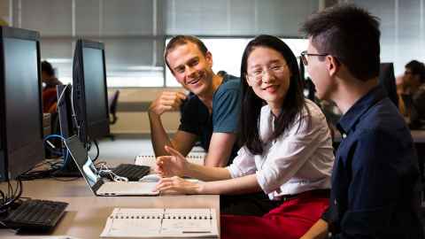 Three people sitting in front of computers, smiling.