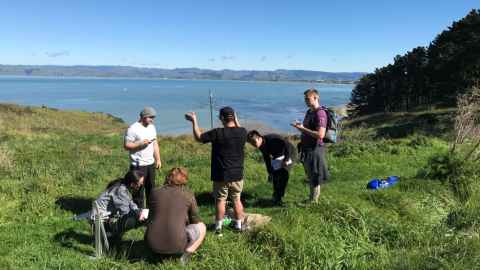 A group of young people on grass near a cliff edge, with sea beyond.