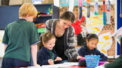 An adult helping children in a classroom.