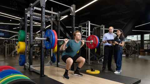 A student weightlifting at Hiwa recreation centre, with tutors standing alongside