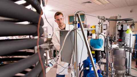A young man in a lab coat and protective glasses, using machinery.
