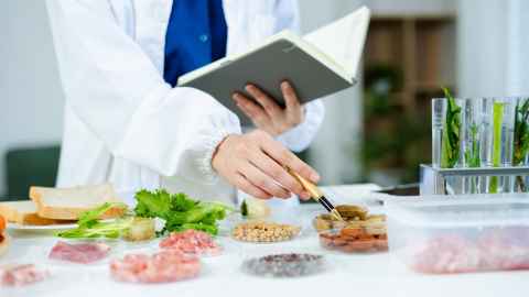 A person holding a notebook, with food and test tubes on a table in front of them.