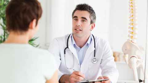 A man in a white coat with a stethoscope around his neck, talking to a woman.