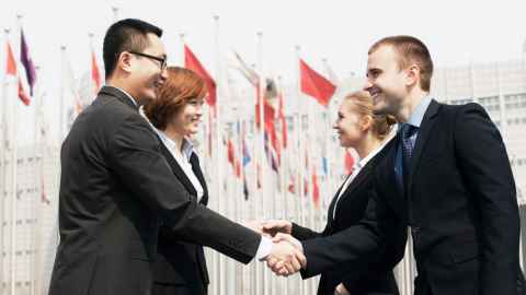 People shaking hands in front of different flags.