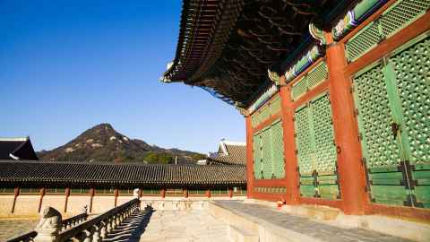 A traditional Asian building with hills and blue sky in the background.