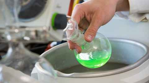 A hand holding a vial of green liquid.