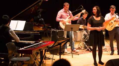 Musicians on stage with guitars, drums, keyboard and piano.