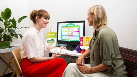 Two people sitting at a desk, with images of food on a computer screen - one of them is holding a plate.