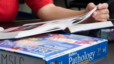 Someone reading a textbook lying on top of another textbook, Rubin's Pathology.