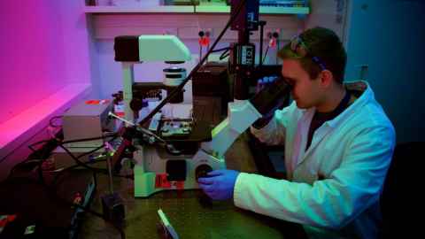 A young man in a white coat looking through a microscope.