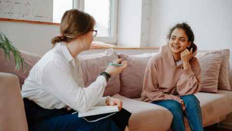 A woman sitting on a sofa with a young girl, talking.