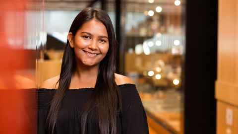 A young woman smiling, leaning on a wall.