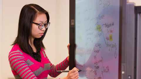 A young woman writing on a whiteboard.