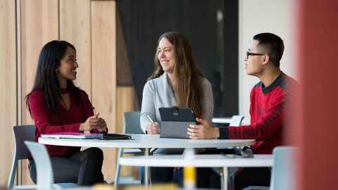 Three people sitting around a study table, smiling.