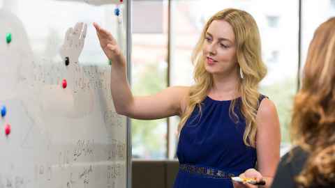 A young woman in front of a whiteboard with equations on it.