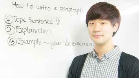 A young man standing beside a whiteboard with writing on 'How to write a paragraph'.