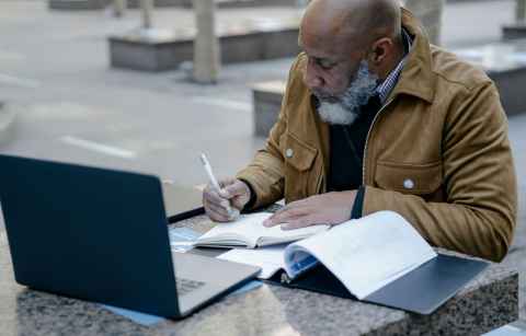 older man writing in a notebook outside