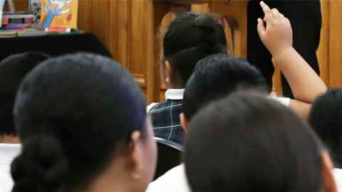 The backs of pacific high school students in a crowd, one in front raises their hand.
