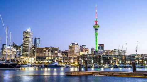 Auckland City skyline at night with the Sky Tower lit up in green and red.