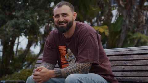 Man with tattoos sitting on a bench smiling at the camera