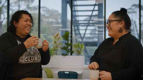 Two woman laughing over a cup of tea together