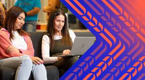 Two women sitting next to each other on a couch looking at a laptop